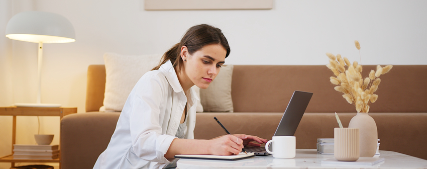 Woman using a computer and writing on a pad.