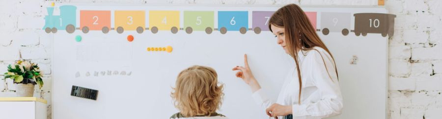 Teacher instructing child in front of whiteboard.